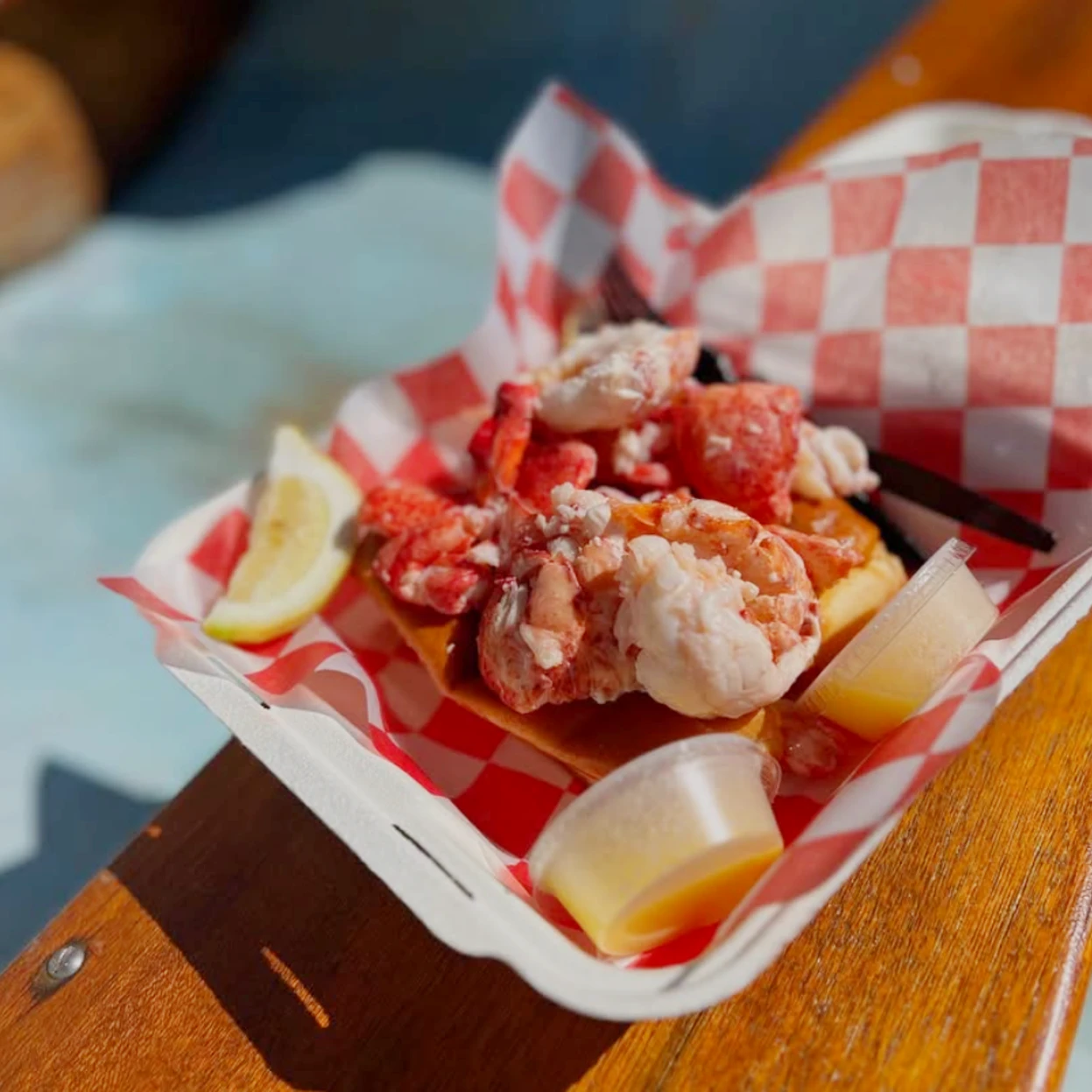A lobster roll with lemon and butter on top of a red and white checkerboard paper.