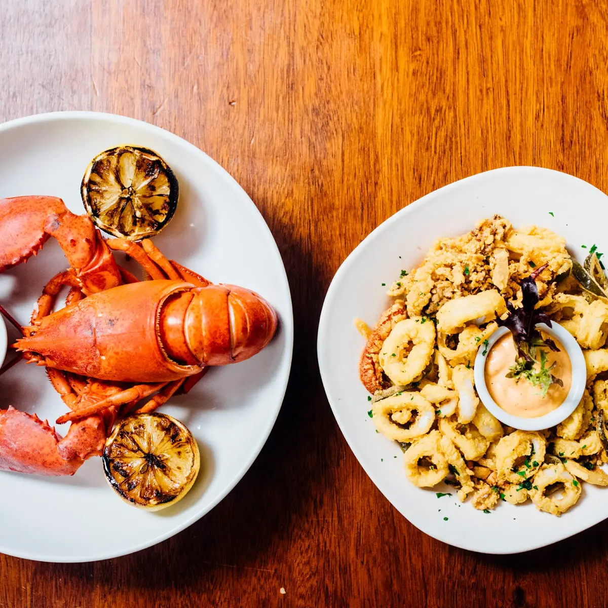 A red boiled lobster and calamari on white plates.