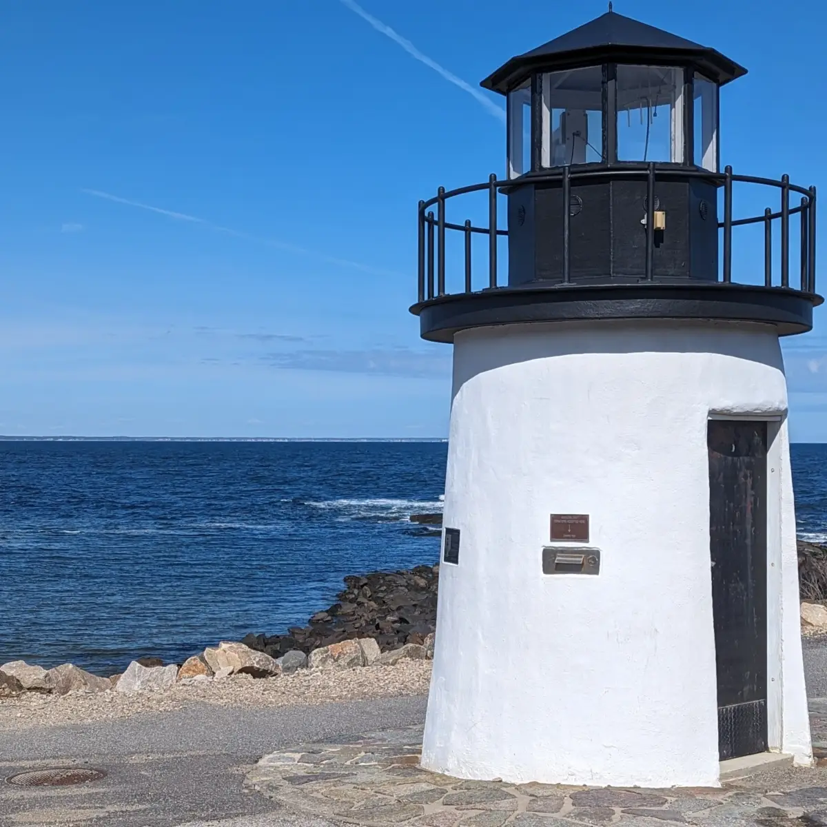 A small white lighthouse with a blue sky behind it.