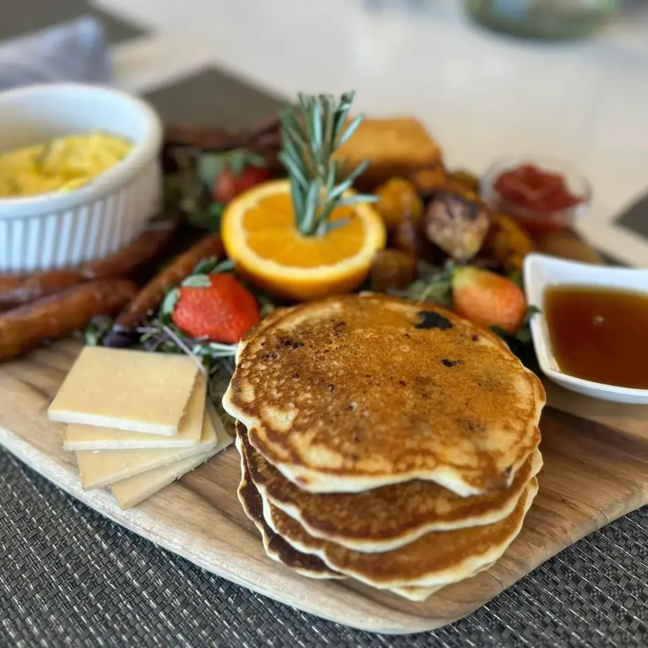 Pancakes, potatoes, fruit, cheese and meats are spread on a wooden board.