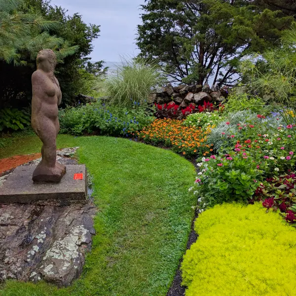 Statue of a woman in a garden surrounded by flowers.
