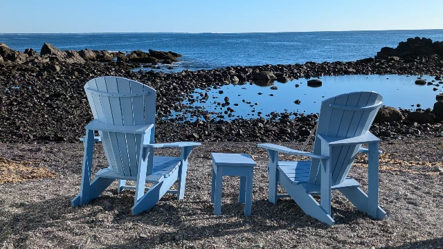 Blue adorondack chairs facing the ocean at Perkins cove.